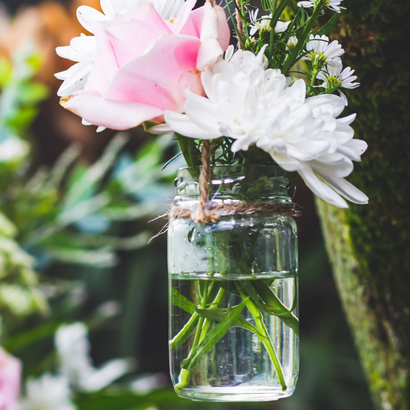 Petit bouquet de fleurs dans les tons rose et blanc, dans un bocal suspendu à un arbre