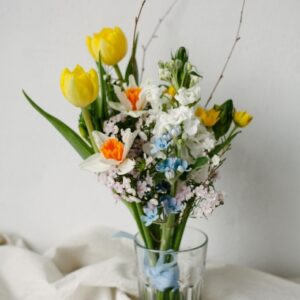 Bouquet de fleurs blanches et jaunes avec une touche de bleu pâle dans un verre